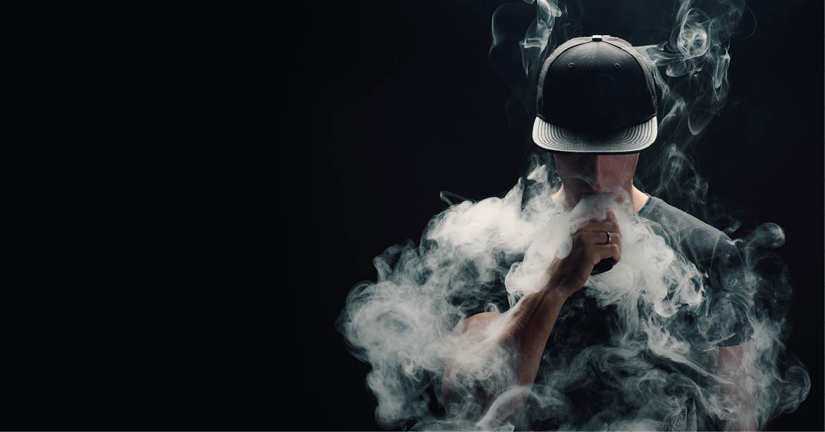 Vape man  Portrait of a handsome young white guy in a modern black cap vaping and letting off puffs of steam from an electronic cigarette 