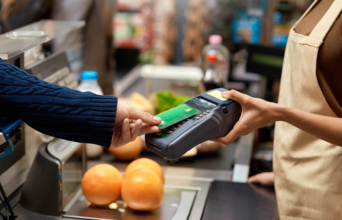 Cropped view of young adult man holding plastic credit card in hand, using terminal and paying for shopping in supermarket