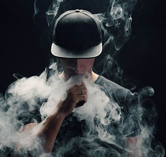 Vape man  Portrait of a handsome young white guy in a modern black cap vaping and letting off puffs of steam from an electronic cigarette 