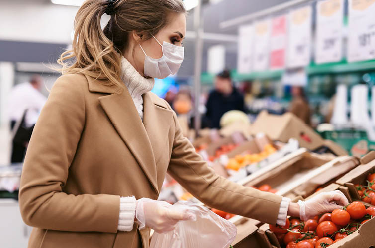 Shopping during the coronavirus Covid-19 pandemic  A young woman buys tomatoes in a supermarket  Woman in facial mask and gloves to prevent infection 