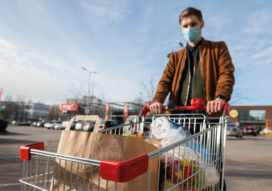 Riga, Latvia - April 20 2020: Grocery shopping Men with face mask during Coronavirus COVID-19 pandemic  Men stockpile food shopping cart outside of a grocery store  Selective focus on groceries