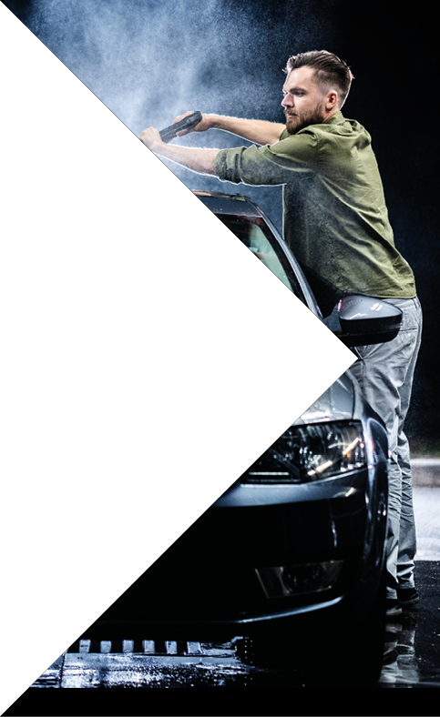 A man with a beard washes a gray car with a high-pressure washer at night in a car wash  Expensive advertising photography
