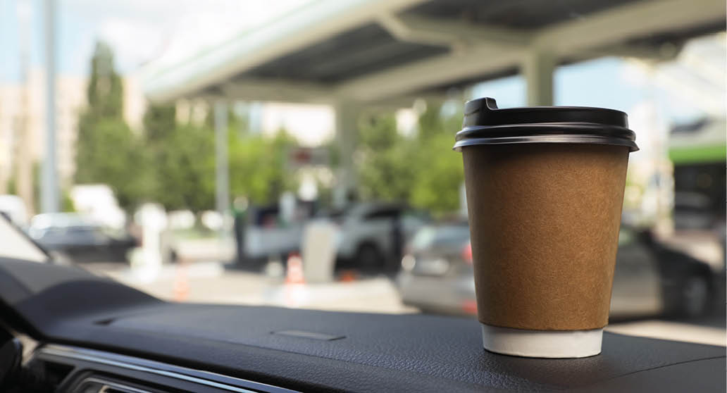 Paper coffee cup on car dashboard at gas station  Space for text