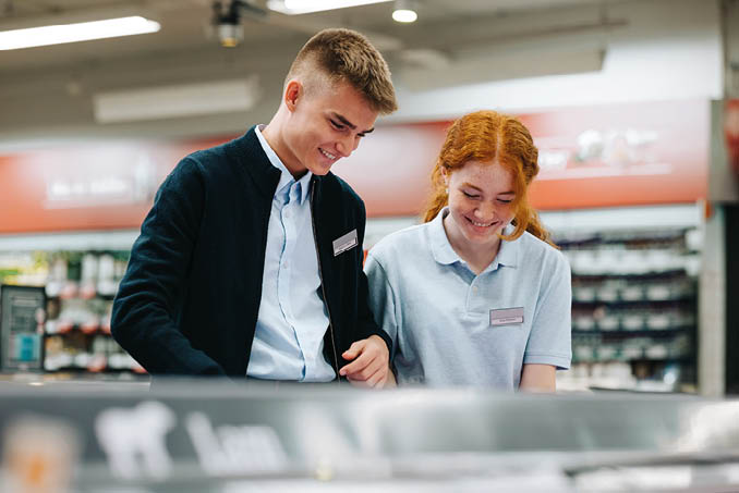 Young man and woman on holiday job at supermarket  Trainees working together in grocery store 