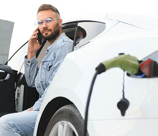 Young stylish man is with electric car at daytime. The concept of green energy.