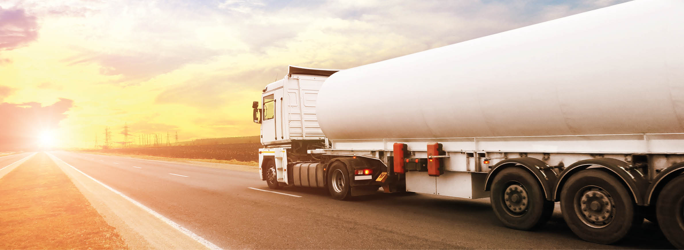 Big metal fuel tanker truck shipping fuel on the countryside road against a night sky with a sunset