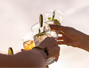 Friends rising cocktail glasses for a celebratory toast against the sky in the summer