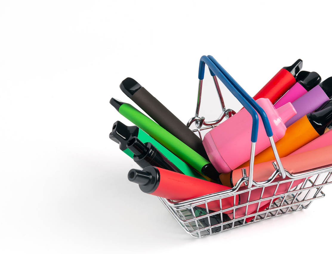 A set of colorful disposable electronic cigarettes of different shapes in a grocery basket on a white background with copy space. Concept of modern smoking.