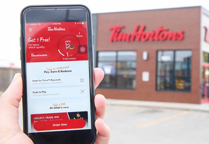 Winnipeg; Manitoba   Canada - October 8; 2019: Close-up of the Tim Hortons App with a Tim Hortons Store in the Background 