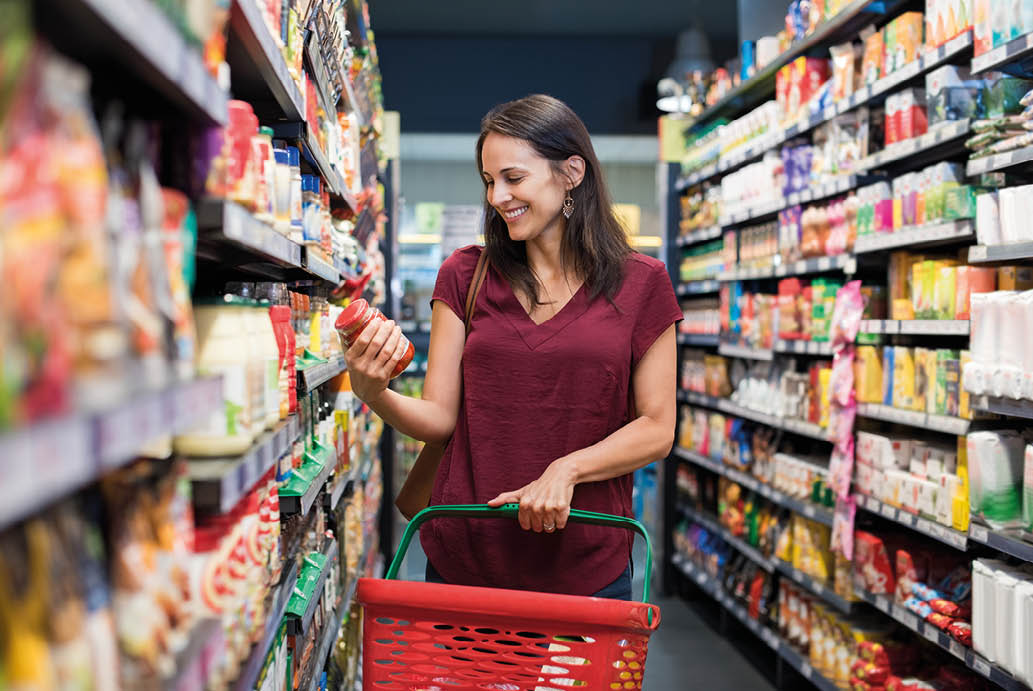 Happy mature woman looking at product at grocery store  Smiling hispanic woman shopping in supermarket and reading product information  Costumer buying food at the market 