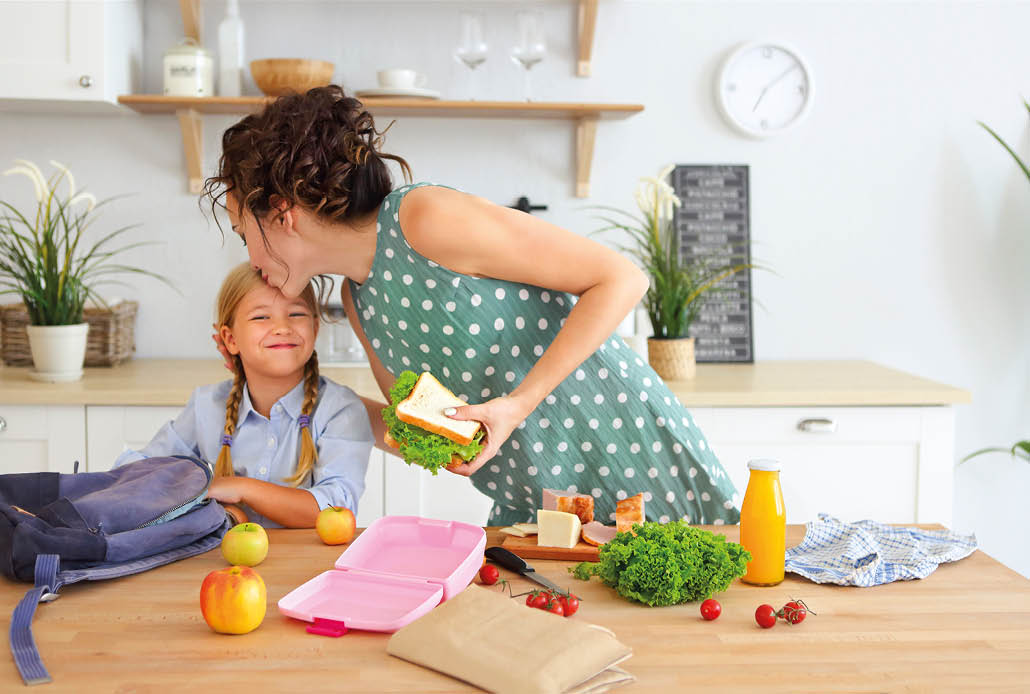 Beautiful brunette mother and her daughter packing healthy lunch and preparing school bag in the kitchen 