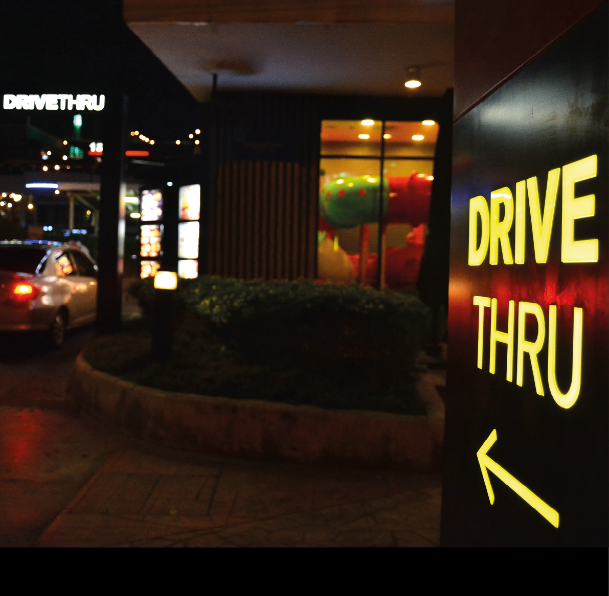 Yellow drive thru sign with an arrow pointer  A car drive into fast food restaurant in the late of night then order some food  Fast food store that open 24 hours selling burger, fried and nugget 