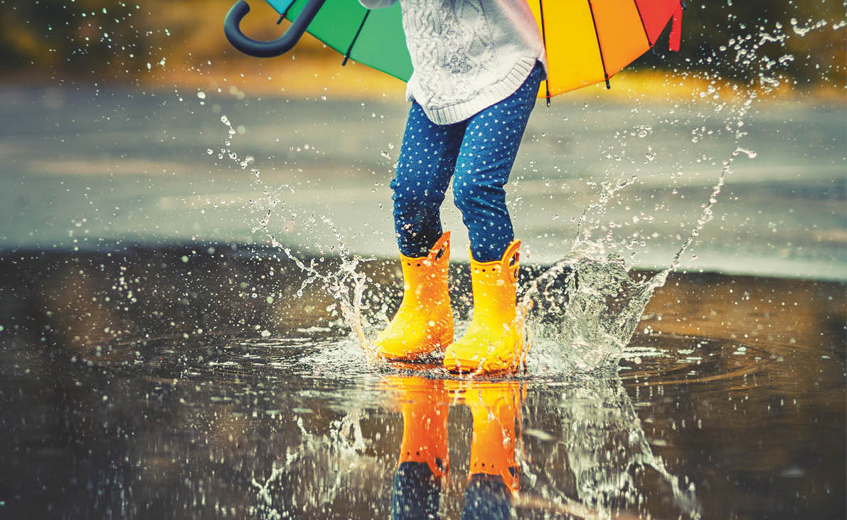 Feet of child in yellow rubber boots jumping over a puddle in the rain