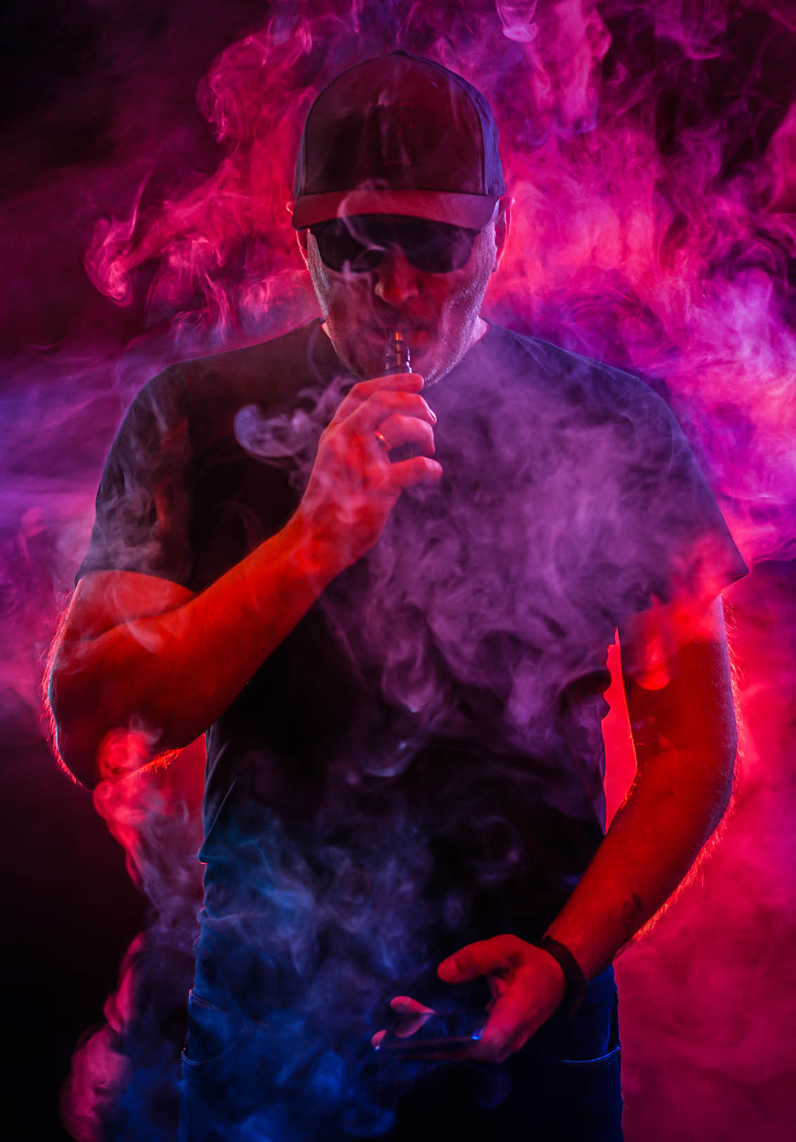 A man smokes an electronic cigarette. The man in the smoke. bearded man vaping. Men with beard in sunglasses vaping and releases a cloud of vapor. vaping man holding a mod. A cloud of vapor. 
