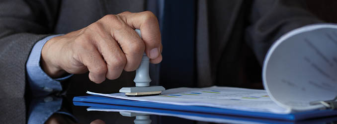 Businessman in suit hand stamping rubber stamp on document at office. Authorized allowance permission approval concept.