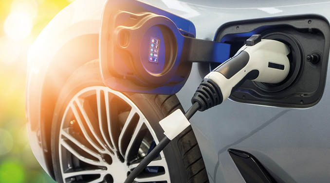 EV Car or Electric car at charging station with the power cable supply plugged in on blurred nature with soft light background. Eco-friendly alternative energy concept