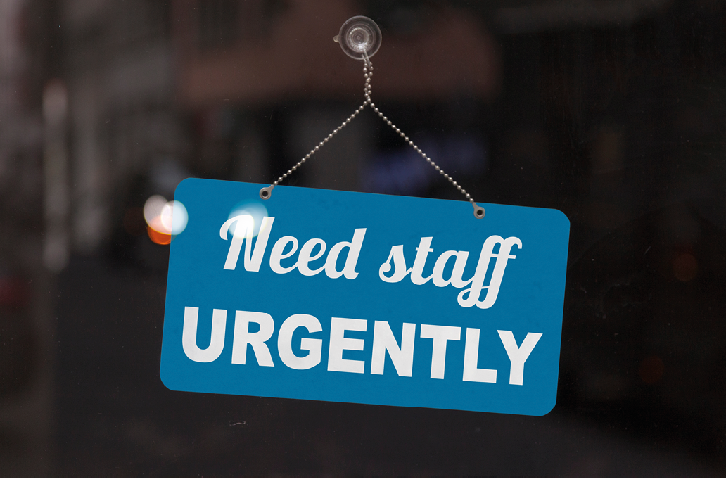 Close-up on a red and white sign in a window with written the message - Need staff urgently - 