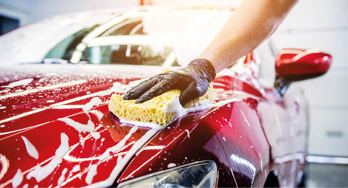 Worker washing red car with sponge on a car wash