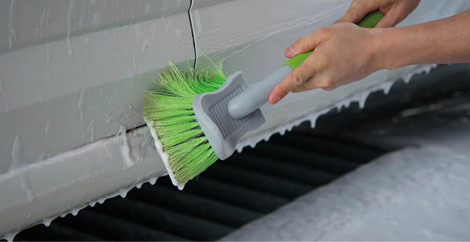 A green brush rubs the foam on the doorstep of a car