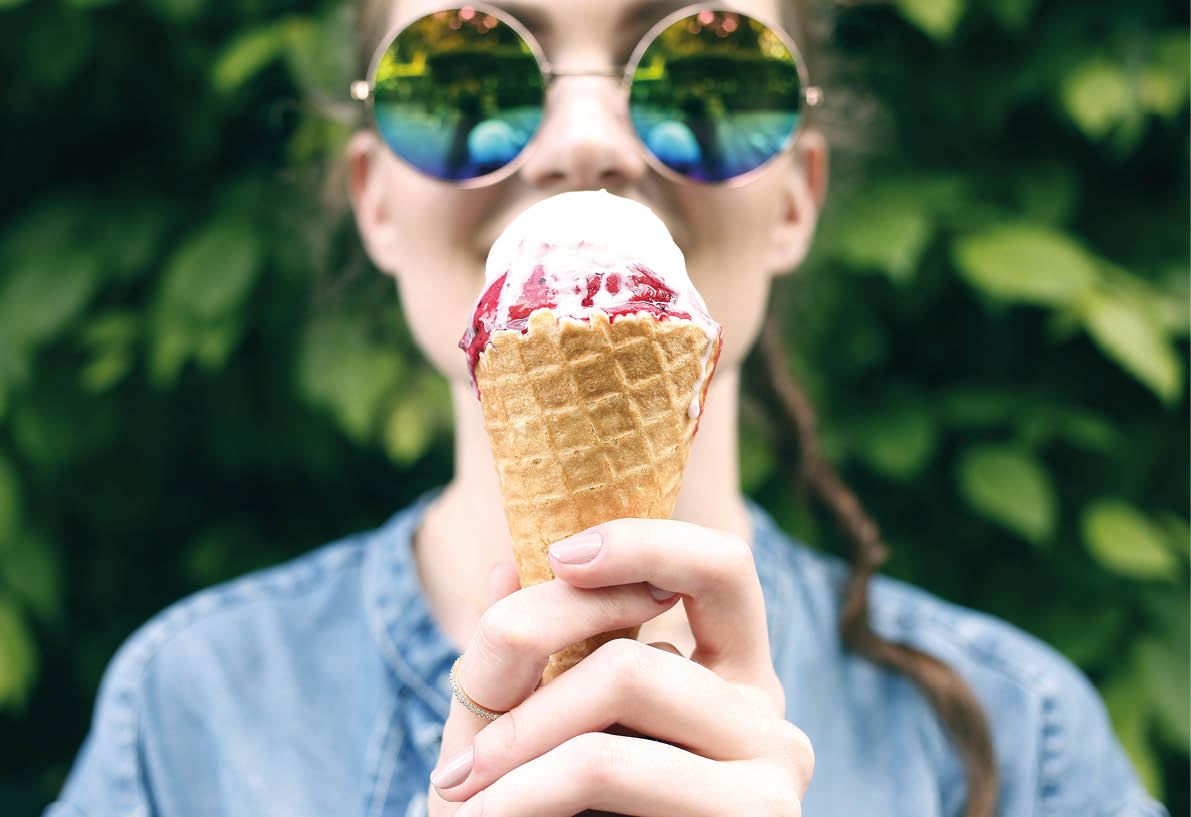 Outdoor closeup fashion portrait of young hipster crazy girl eating ice cream in summer hot weather in round mirror sunglasses have fun and good mood. Toned style instagram filters
