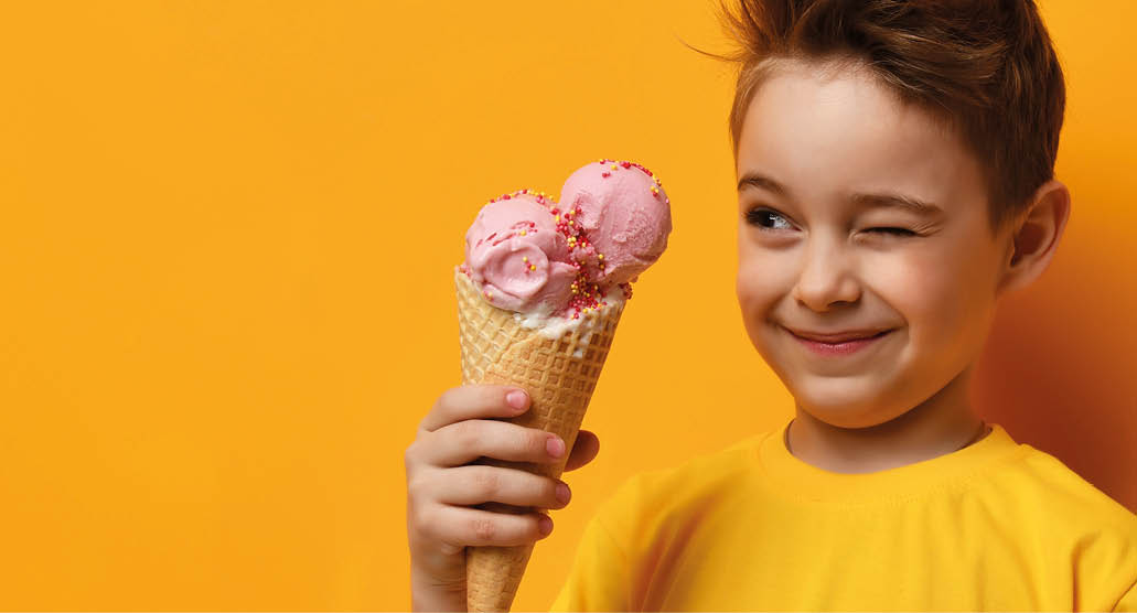 Baby boy kid eating strawberry ice cream in waffles cone and winking on yellow background with free text copy space
