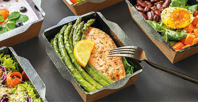 Ready healthy food catering menu in lunch boxes fish and vegetable packages as daily meal diet plan courier delivery with fork isolated on black table background. Take away containers order concept.