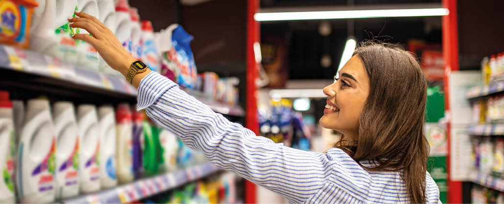 Young smiling woman groceries shopping in local supermarket. She always compares brands and prices. Beautiful caucasian woman shopping personal hygiene products at supermarket.
