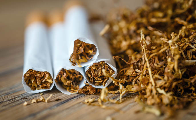 cut tobacco leaves and handmade cigarettes on a wooden background