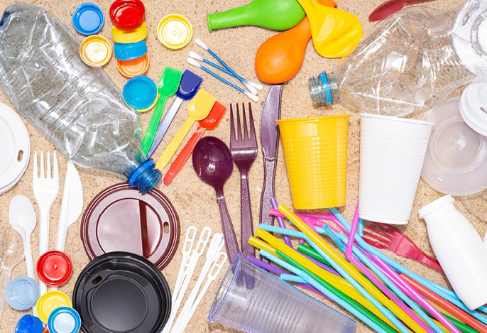 Disposable single use plastic objects such as bottles, cups, forks, spoons and drinking straws that cause pollution of the environment, especially oceans  Top view on sand
