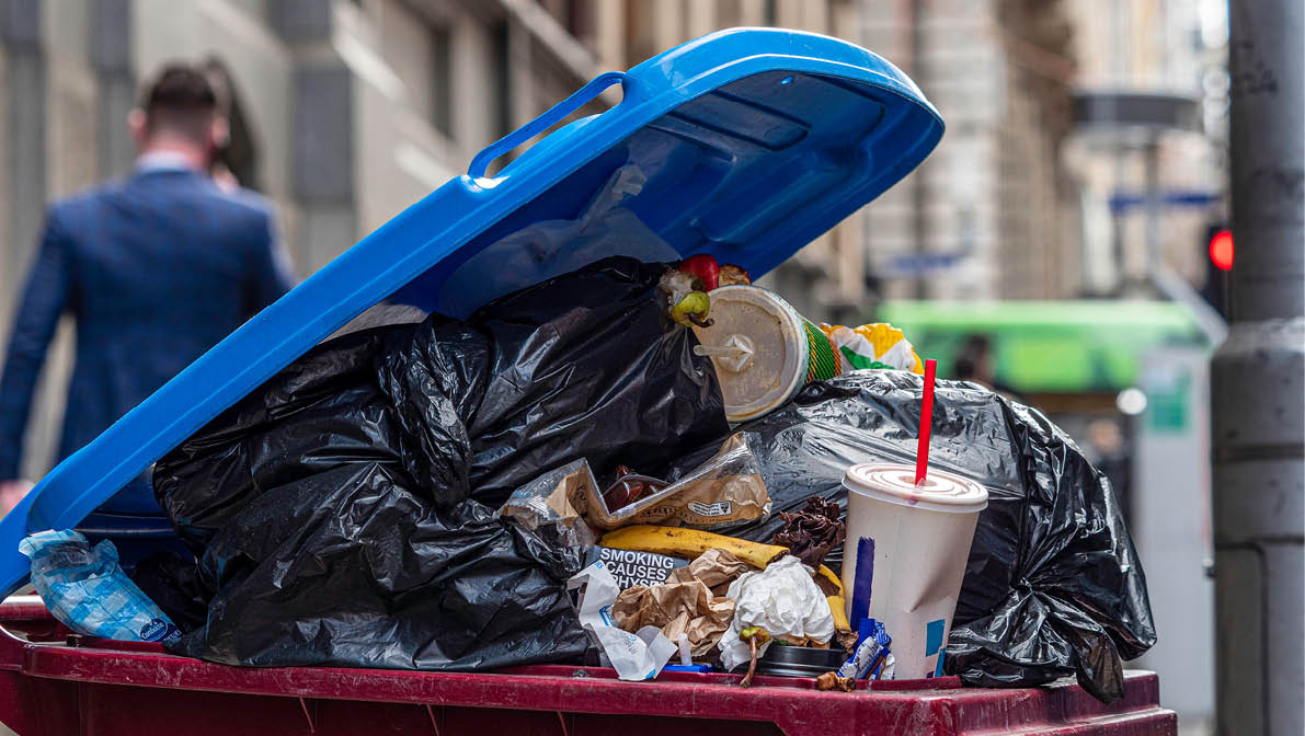Urban rubbish bin overflowing in a populous city  Food scraps, plastic waste, single use bags  Shows recycling problems or issues, waste management, etc  Melbourne, Australia - September 2019: 