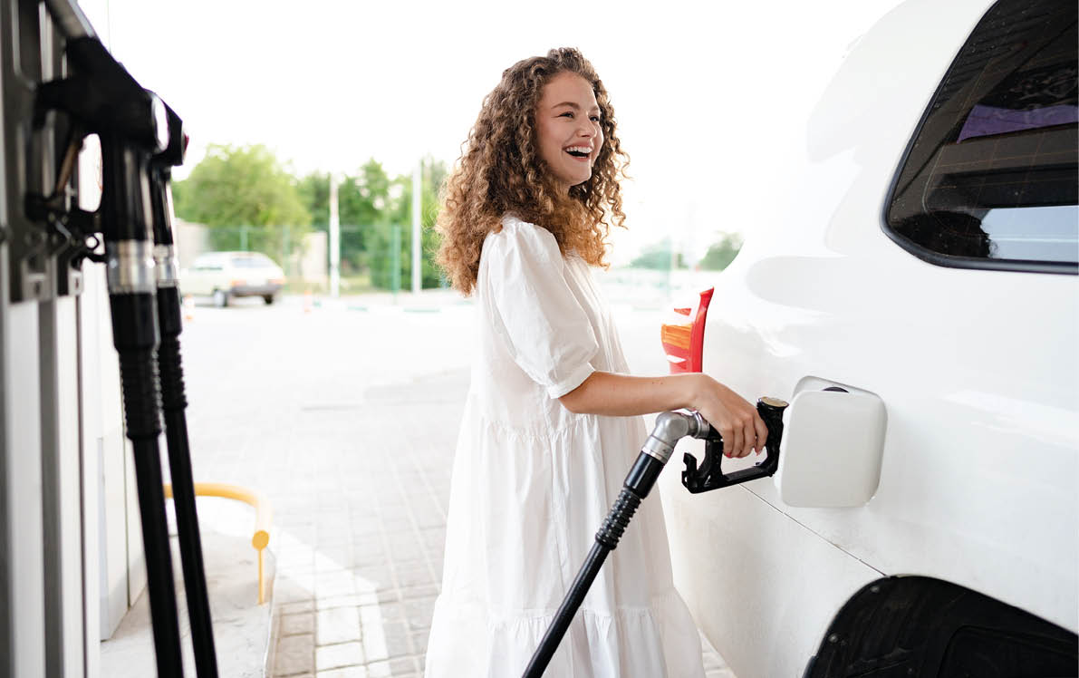Young curly woman refueling car at gas station