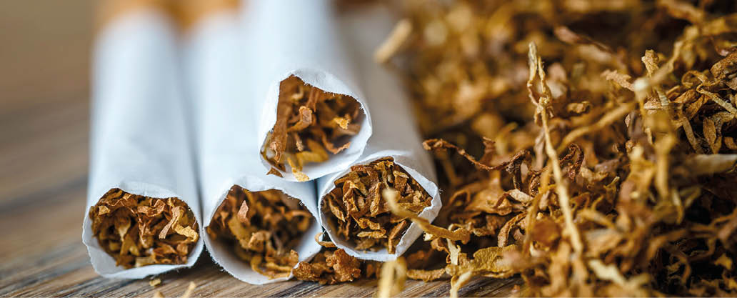 cut tobacco leaves and handmade cigarettes on a wooden background