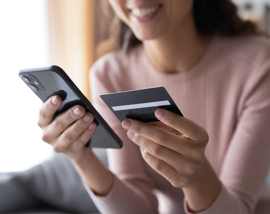 Close up smiling millennial woman holding smartphone and banking credit card, involved in online mobile shopping at home, happy female shopper purchasing goods or services in internet store.