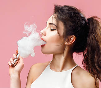 Casual pretty woman standing and vaping on pink background in studio.