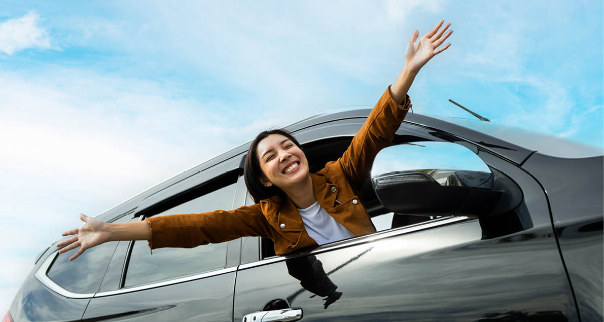 Young beautiful asian women getting new car. she very happy and excited. Smiling female driving vehicle on the road on a bright day. Sticking her head outta the windshield