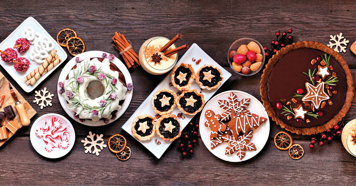 Assorted Christmas holiday desserts and sweets. Top view panoramic table scene over a rustic wood background. Bundt cake, chocolate pie, mincemeat tarts, cookies, fudge and eggnog.