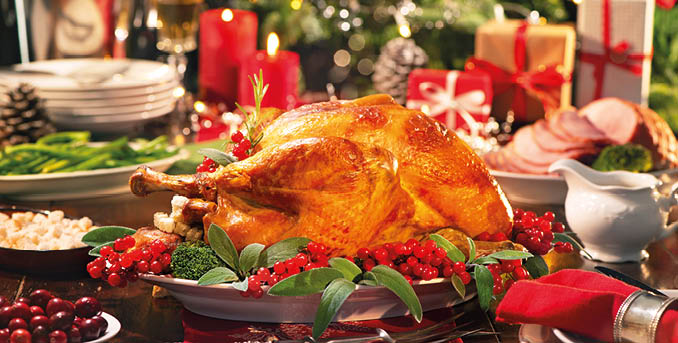 Christmas turkey dinner. Baked turkey garnished with red berries and sage leaves in front of Christmas tree and burning candles