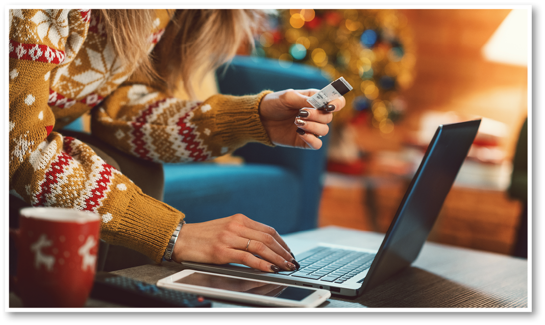 Woman doing online shopping at Christmas: she is sitting on the sofa at home, connecting with her laptop and holding a credit card, Christmas tree in the background