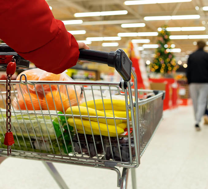 Woman with a basket walks in a supermarket. Hand and part of the basket in focus, blurred background