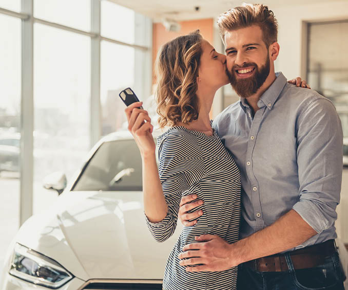 Visiting car dealership  Beautiful couple is holding a key of their new car and smiling, girl is kissing her husband in cheek