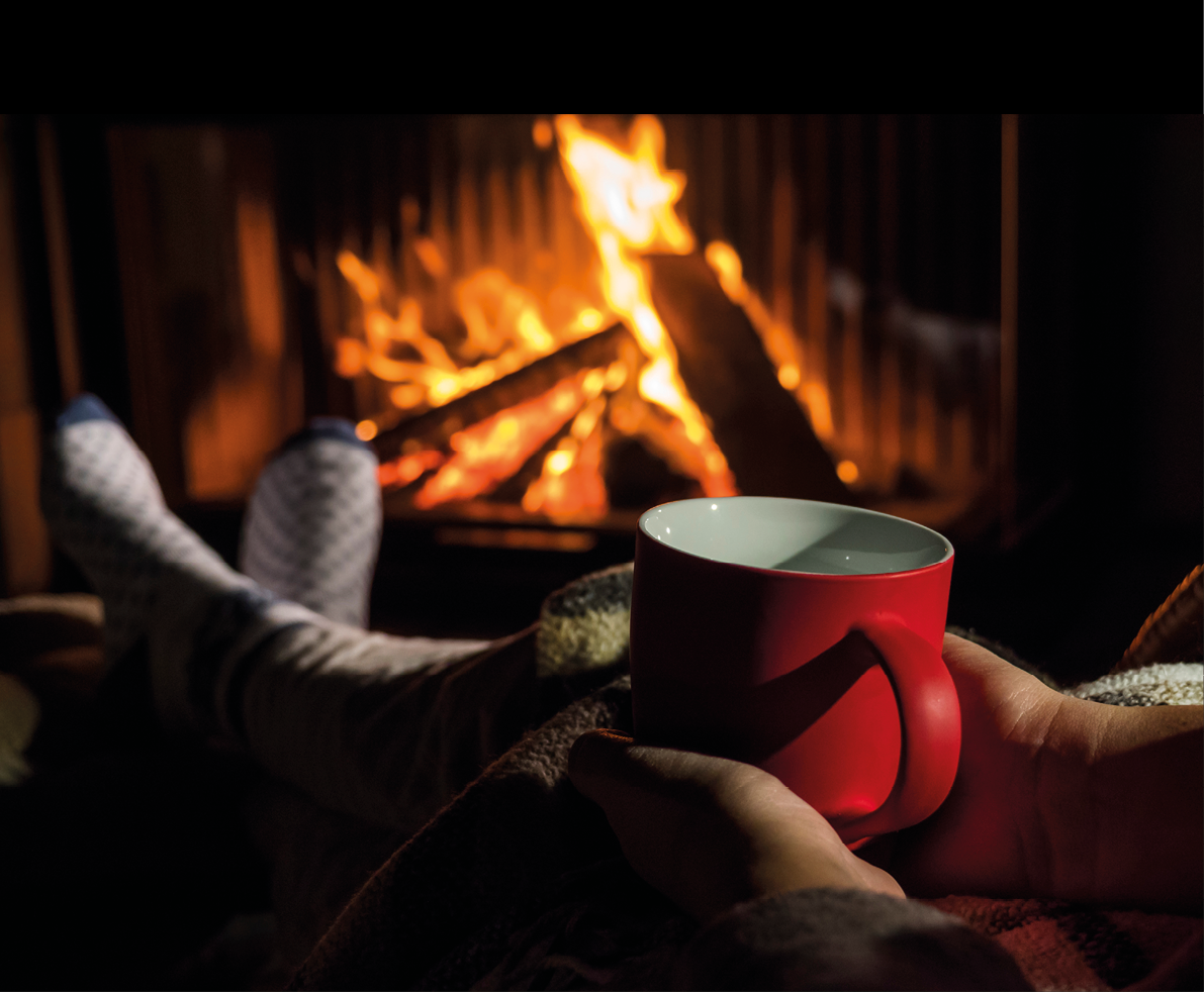 Woman with a red cup of tea is relaxing by the fireplace