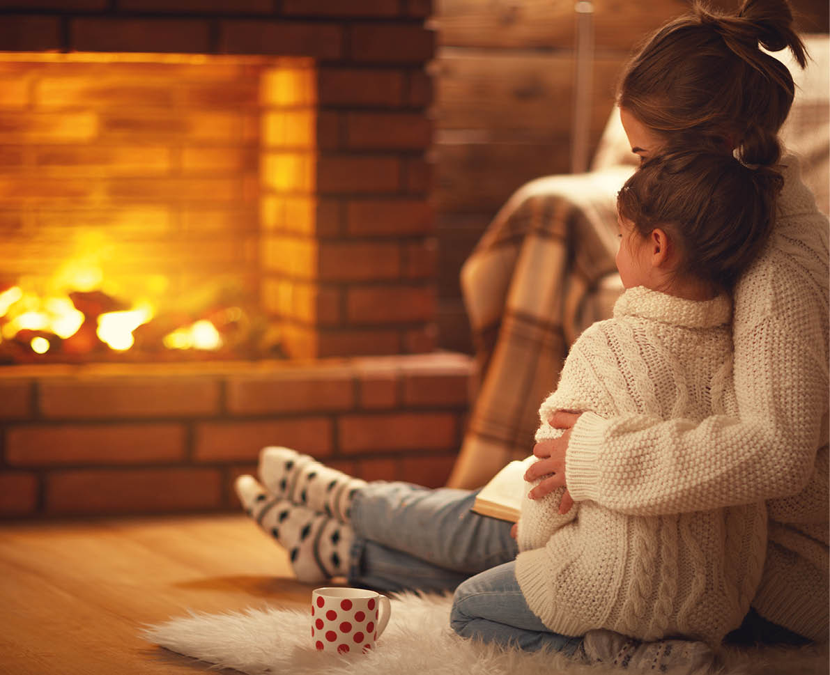 family mother and child daughter hugs and warm on winter evening by fireplace