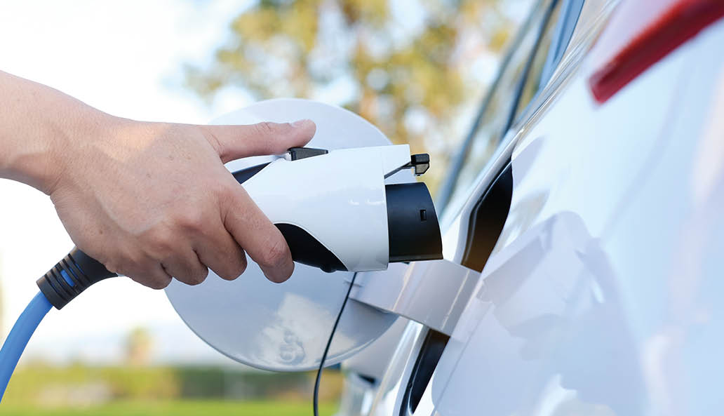 Electric car or ev is charging at station . man use the white power cable and plug on nature background. eco and clean energy concept with the mobile phone smart technology. zero gas no transmission