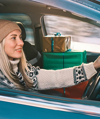 Woman Giving Gifts. Female is holding presents and delivering them on her car to Home. Holidays concept. Driving car in Christmas Eve. People In A Snow-Covered Forest. Sunny Cold Winter Day.