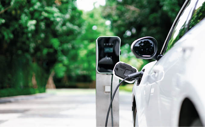 Focus closeup electric vehicle plugged in with EV charger device from blurred background of public charging station powered by renewable clean energy for progressive eco-friendly car concept.