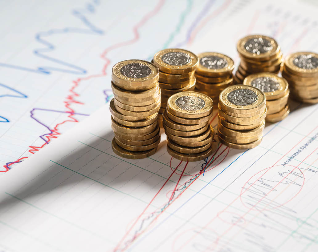 Stack of pound coins on financial graphs and figures balance sheet