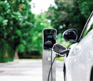 Focus closeup electric vehicle plugged in with EV charger device from blurred background of public charging station powered by renewable clean energy for progressive eco-friendly car concept.