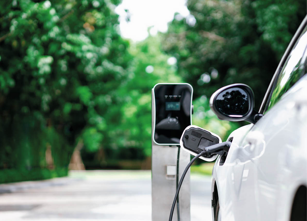 Focus closeup electric vehicle plugged in with EV charger device from blurred background of public charging station powered by renewable clean energy for progressive eco-friendly car concept.