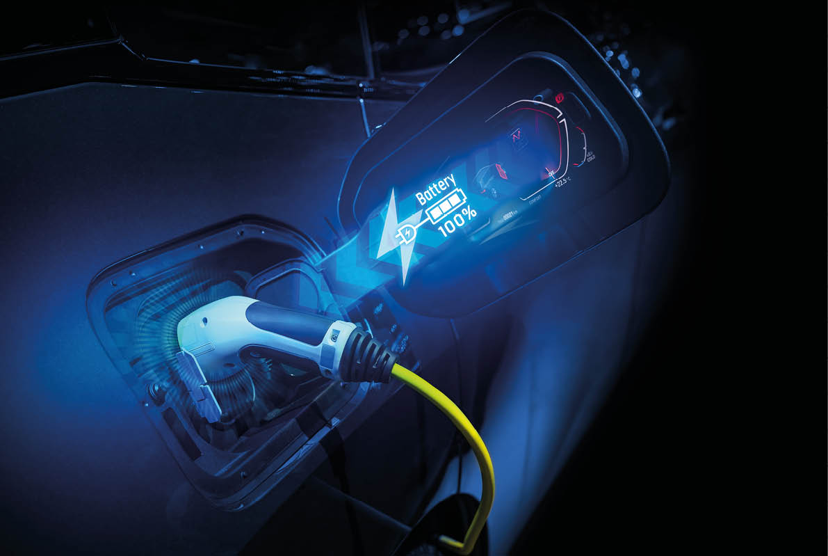 An electric vehicle is being charged with a yellow cable connected to the charging port, accompanied by a digital overlay showing the battery at 100% charge. Description generated by AI