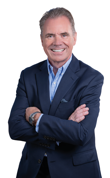 A person with short hair is smiling and wearing a dark blue suit jacket over a light blue striped shirt with arms crossed against a white background. Description generated by AI